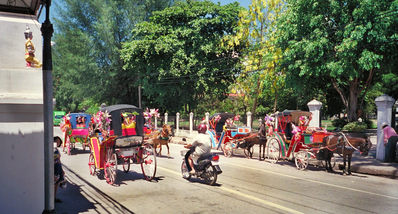 南邦道路旁停靠多輛彩色馬車，前方有機車經過