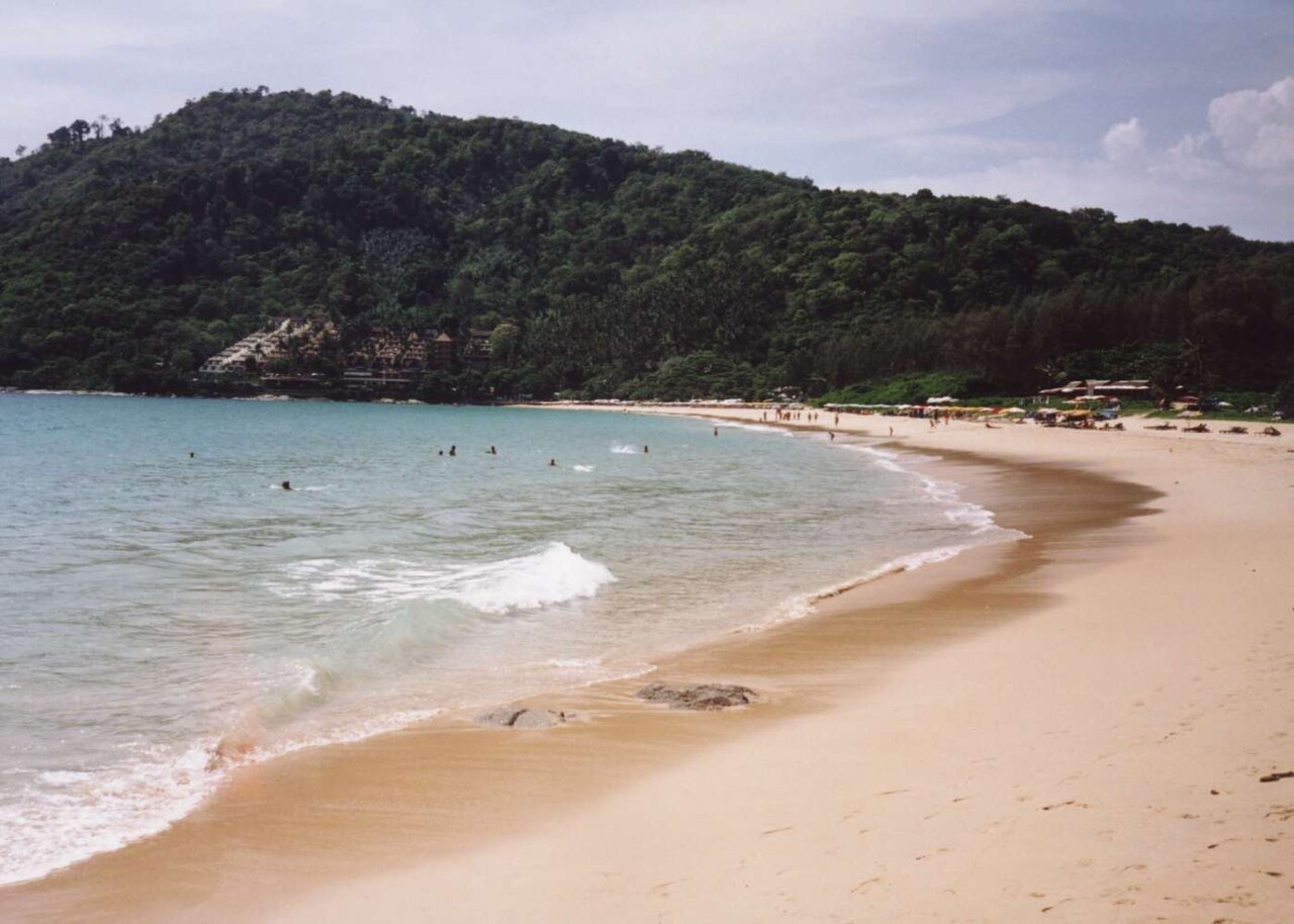 普吉奈漢海灘的弧形海岸與綠色岬角，呈現目的地環境而非 Paresa 或 The Nai Harn 飯店景觀